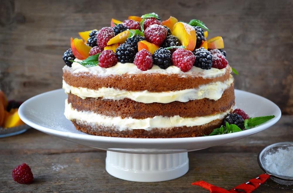 Naked cake with cream, decorated with raspberries, blackberries, peaches
