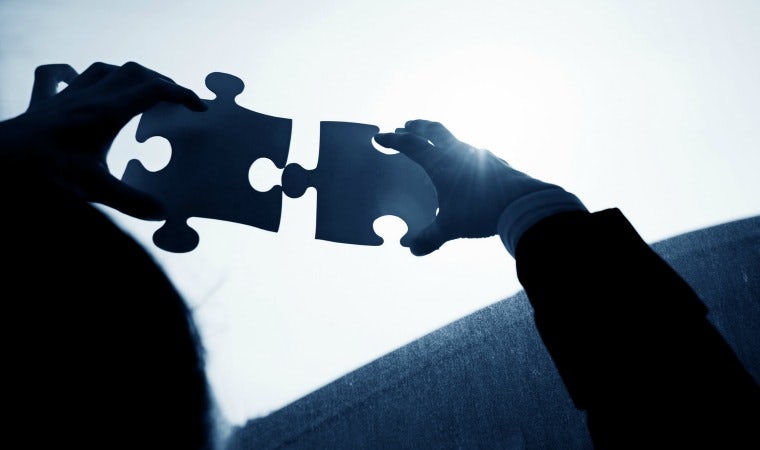 Woman hands connecting two jigsaw puzzle pieces against sunset sky.